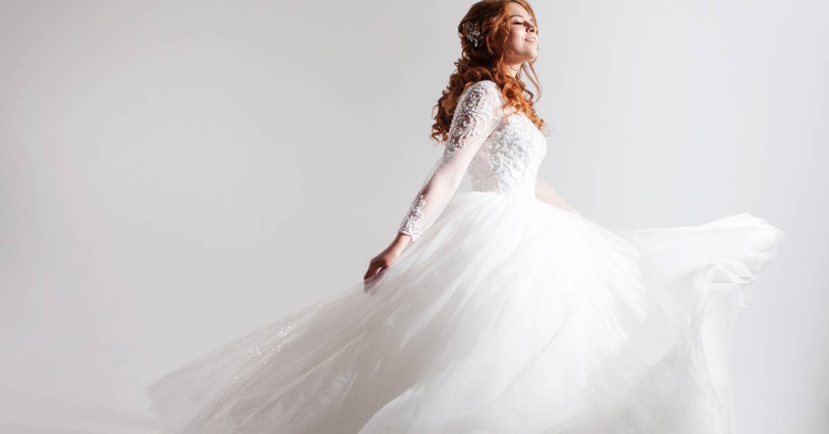 A bride's side profile; she has her eyes closed and her arm stretched out. The bottom of the dress poofs out.