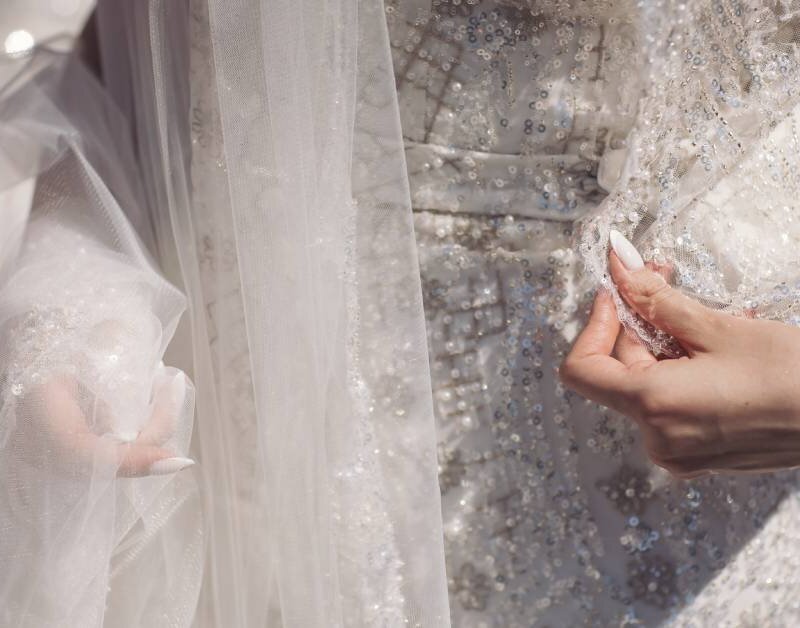 A close-up of an elegant white dress with embroidered flowers. The woman shows off the details in the dress.