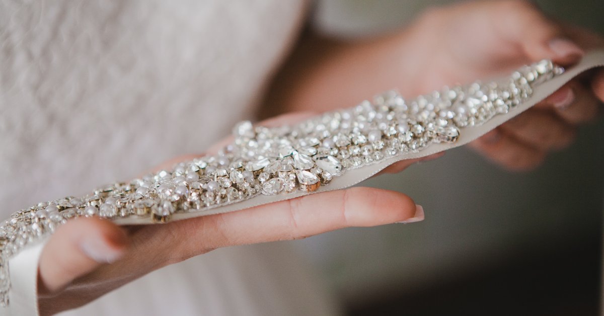 A close-up shot of a bride holding a belt with rhinestones. The jewelry sparkles and the small details are highlighted.