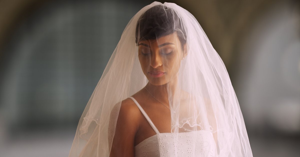 A portrait of a bride dressed in her wedding gown with her veil covering her upper body. She is wearing a necklace.